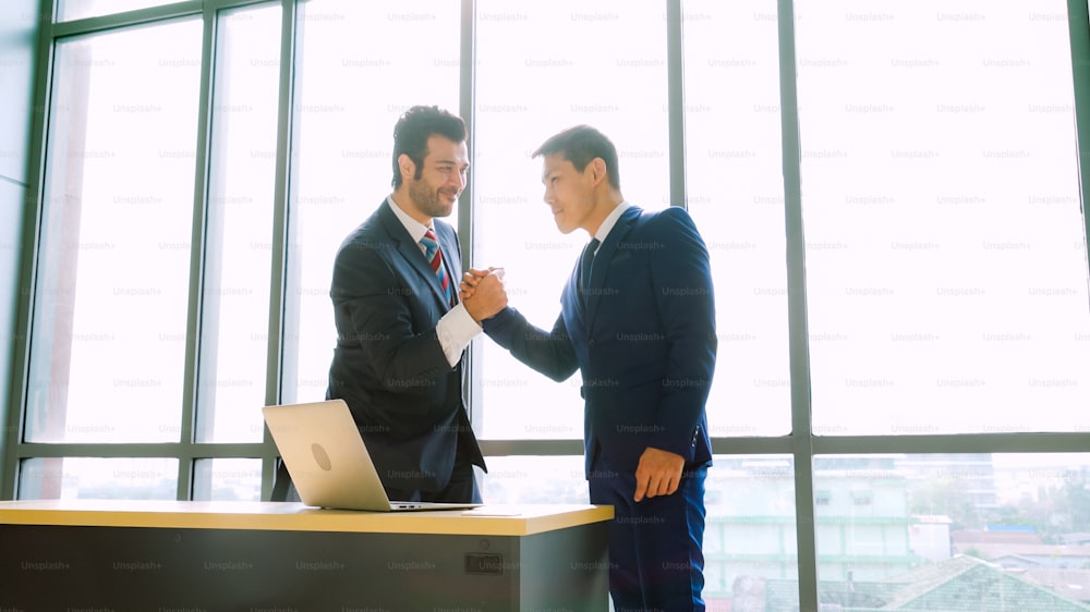 Two happy business people celebrate at office meeting room. Successful businessman congratulate project success with colleague at modern workplace while having conversation on financial data report.