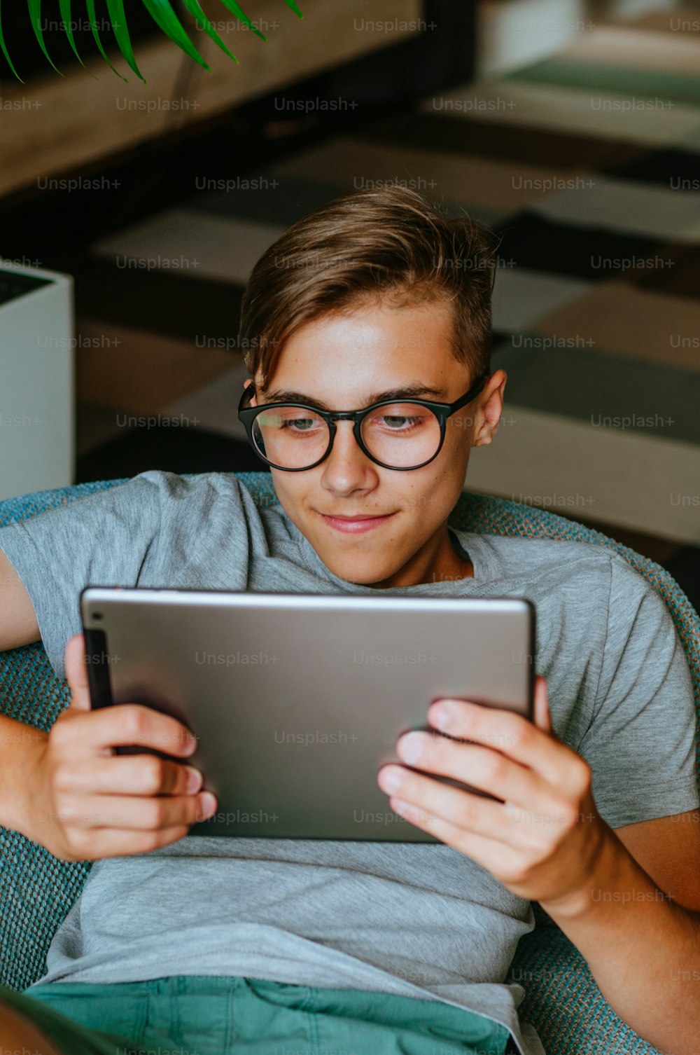 Smiling teenager boy using tablet enjoying communication sitting in the chair indoor.