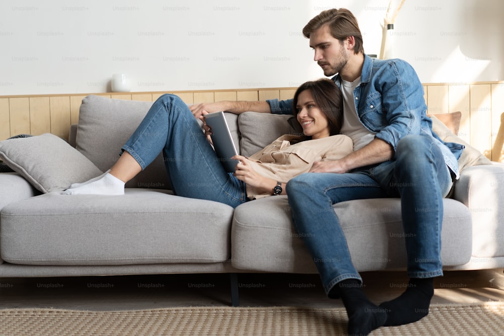 Young couple sitting on couch at home, using a tablet PC for Internet and social media