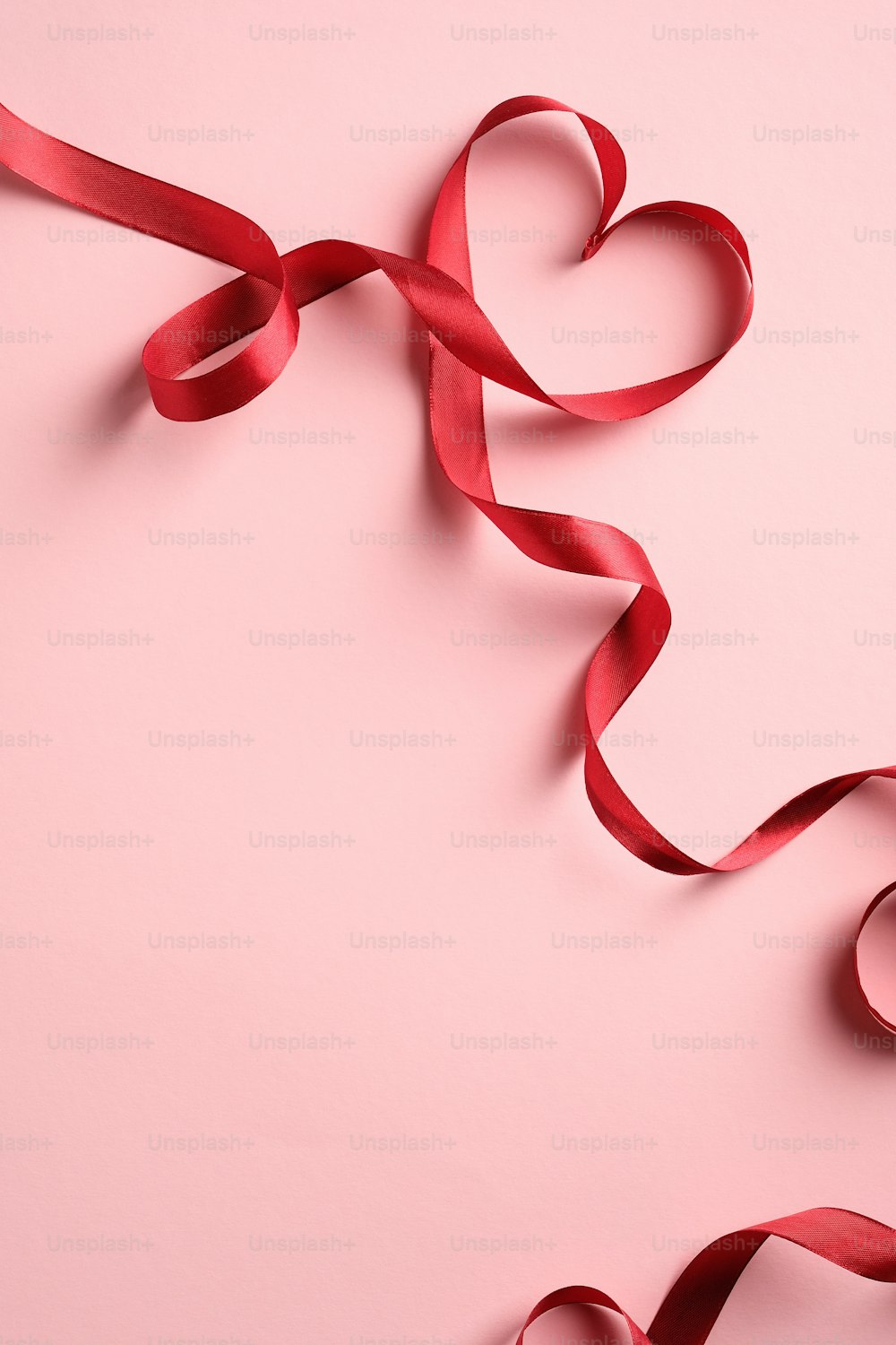 Rotes herzförmiges Band auf rosa Hintergrund. Happy Valentinstag oder Muttertagskonzept.