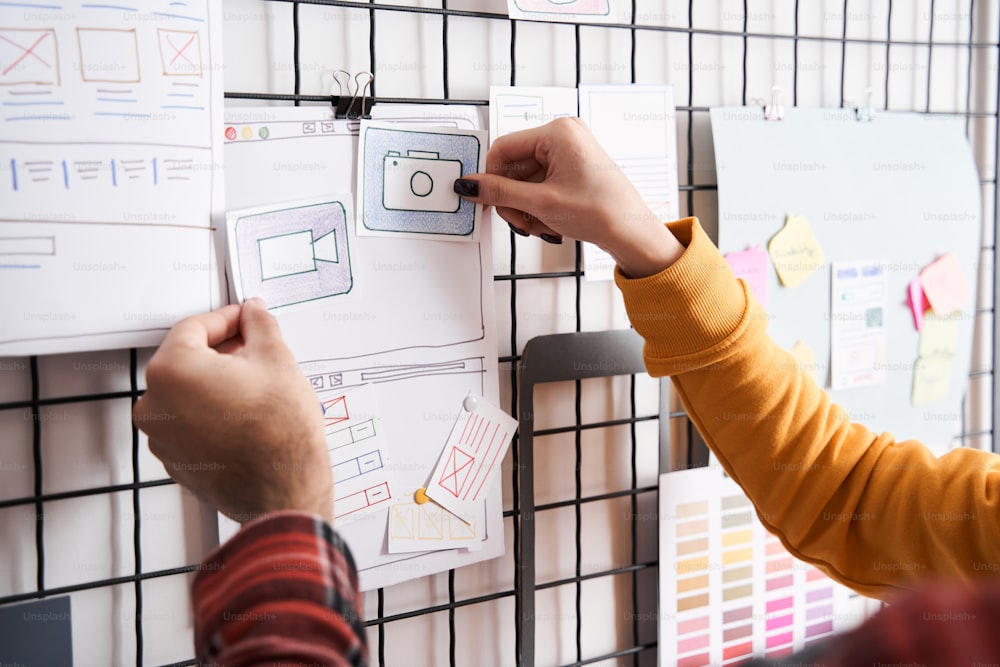 Cropped view of the specialists creating a prototype user experience interface, while standing near the board and discussing. Creative web application development for a smartphone concept