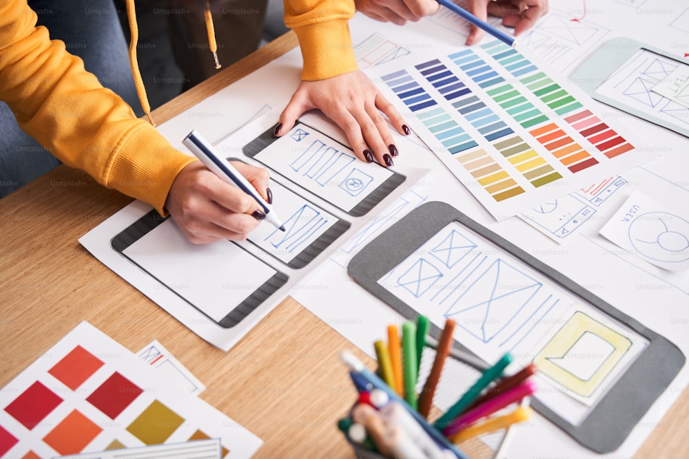 Website designer creating a sketch application. People developing a project while drawing an interface mockup, standing at the table