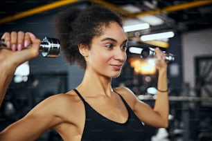 Positive delighted female person keeping smile on her face while working at her perfect body