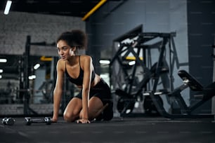 Pretty sportswoman leaning hands on floor while breathing deep after lifting dumbbells
