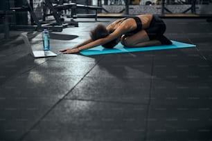 Giovane donna bruna che mette la testa sul tappetino mentre fa esercizio di stretching