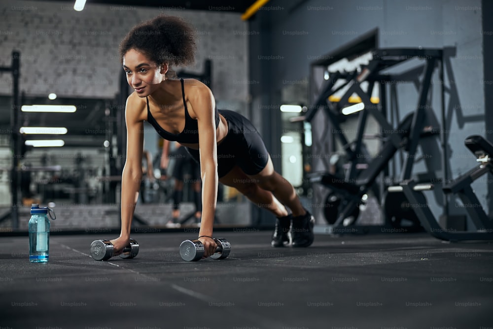 Kind sportswoman leaning on dumbbells while looking forward during workout