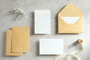 結婚式の招待状と文房具の上面図。白紙のカードのモックアップ、クラフト紙の封筒、リボン、石のテーブルの上の花。ビンテージスタイル。フラットレイ。