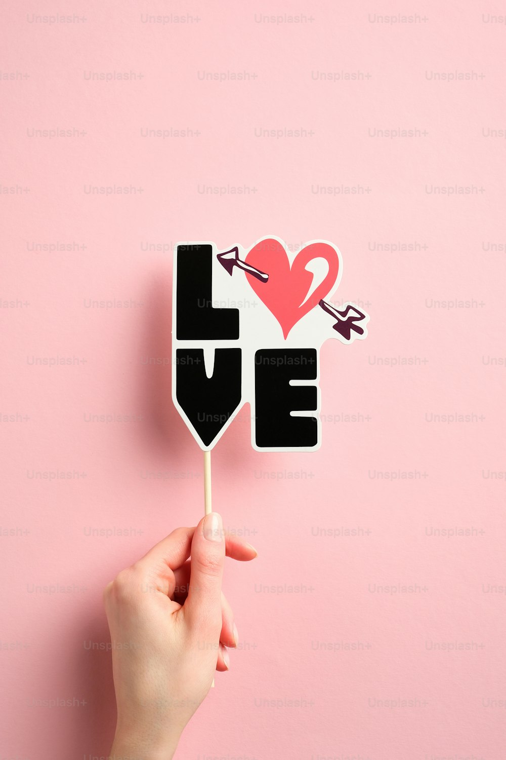 Woman's hand holding Valentines day decoration with sign LOVE over pink background. Top view.