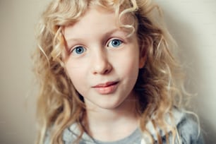 Closeup portrait of beautiful smiling Caucasian blonde girl with long hair on light neutral beige background. Pretty real girl child with natural emotions. Happy authentic childhood lifestyle.