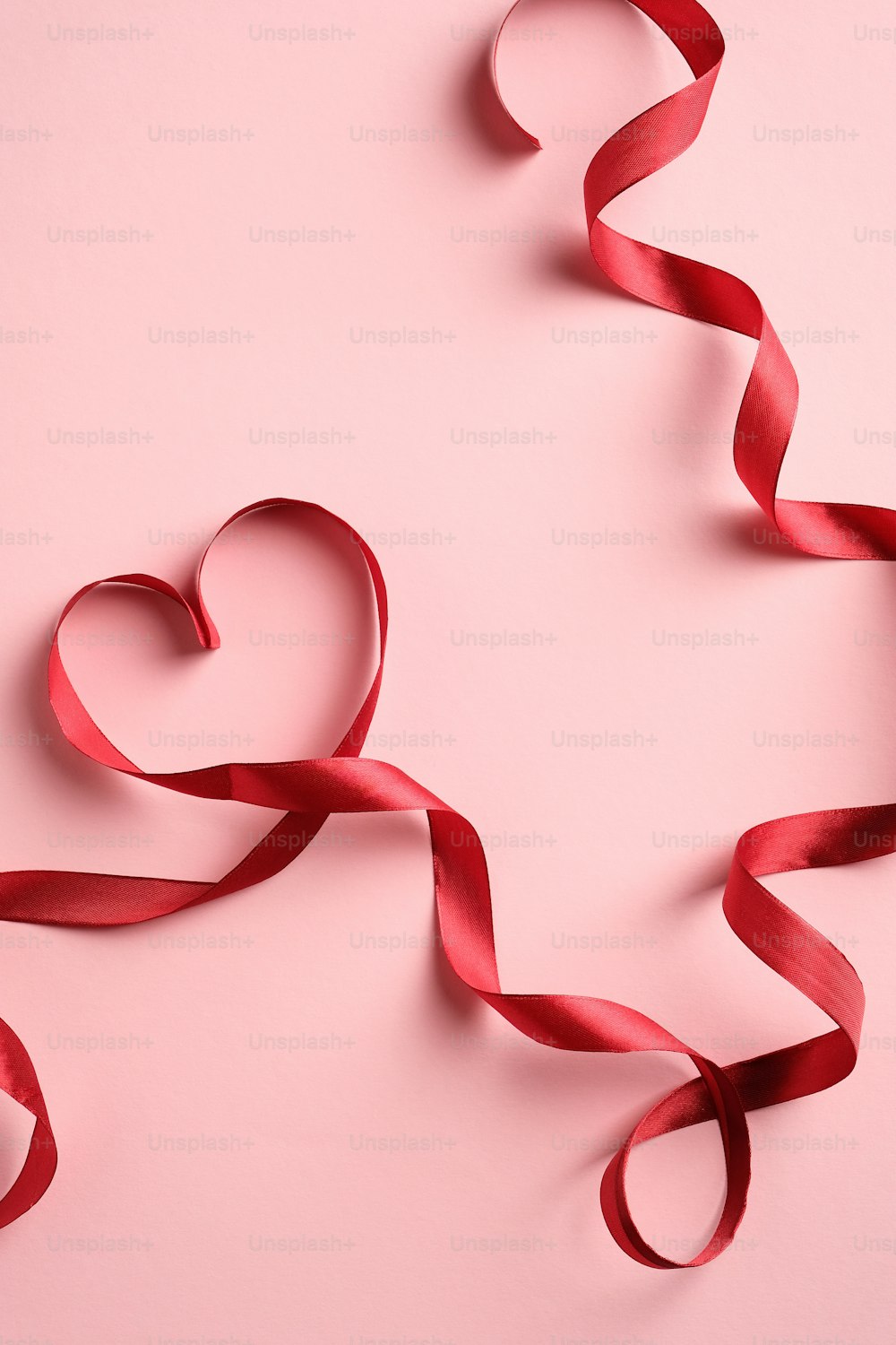 분홍색 배경에 하트 모양의 빨간 리본. 사랑, 로맨스 개념. 발렌타인 데이 또는 어머니의 날 인사말 카드 템플릿입니다.