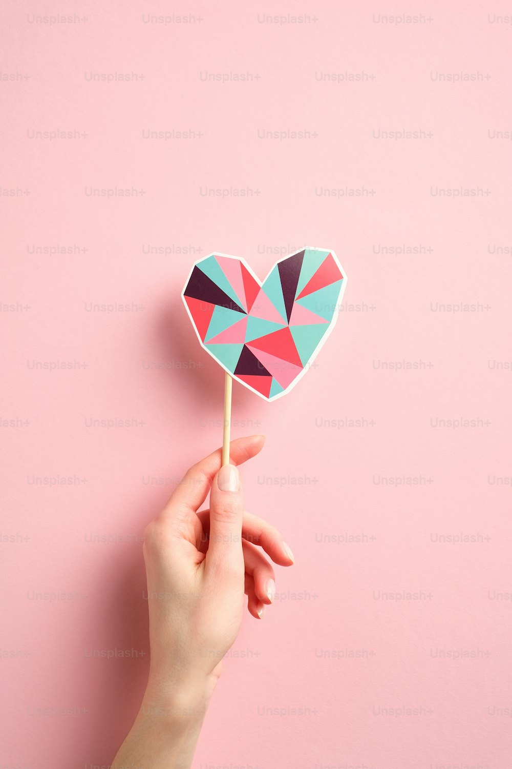Woman's hand holding heart shaped decoration over pink background. Minimal style. Happy Valentines day concept.