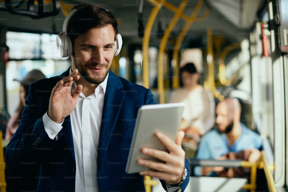 Happy entrepreneur using touchpad and waving during having video call while commuting to work by bus.