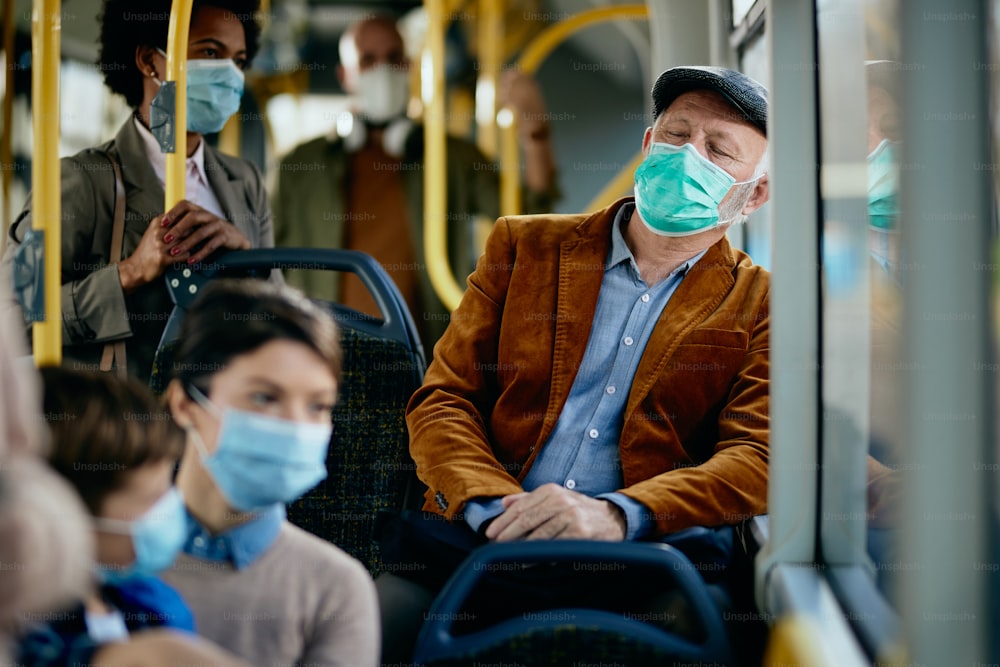 Homem idoso sonolento com máscara facial apoiada em uma janela e descansando enquanto viaja de transporte público.