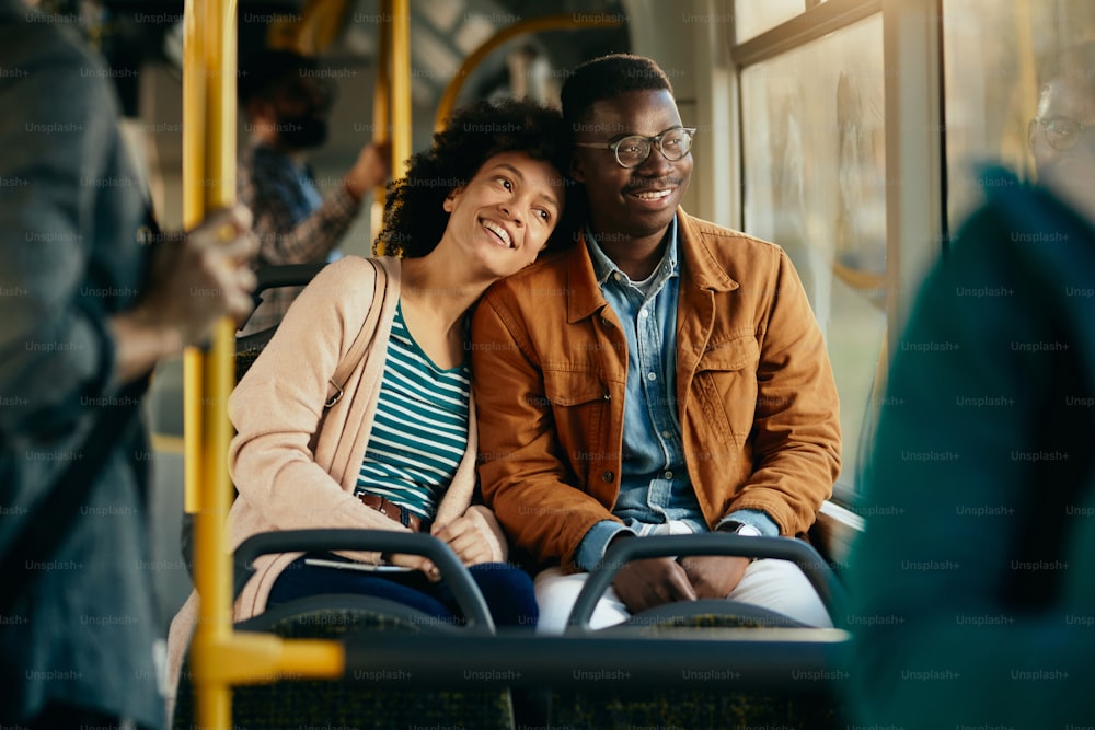 Glückliches schwarzes Paar, das durch das Fenster schaut, während es mit öffentlichen Verkehrsmitteln pendelt.