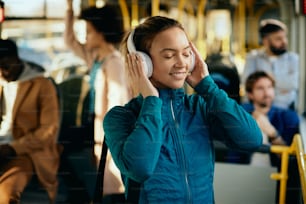 Atleta feminina feliz desfrutando de música através de fones de ouvido enquanto se desloca de ônibus.
