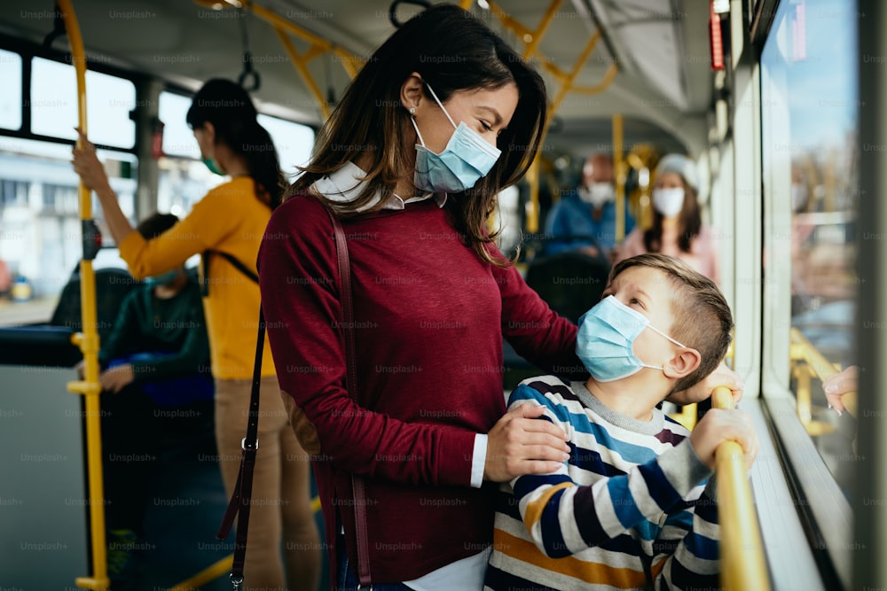 Mãe feliz se comunicando com o filho enquanto se desloca de transporte público e usa máscaras faciais devido à pandemia de COVID-19.