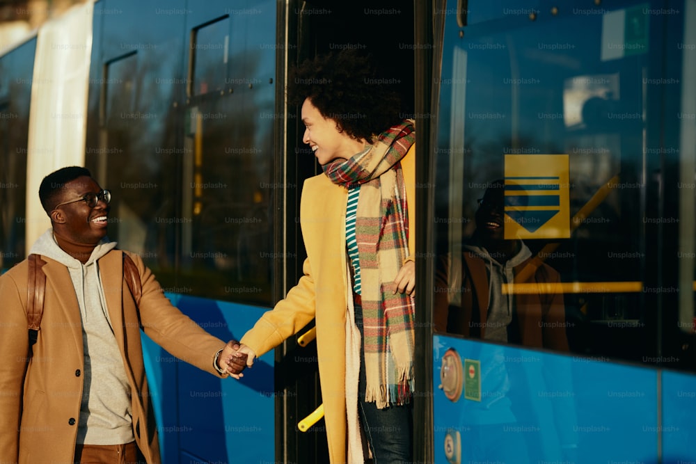 Happy African American woman holding hands with her boyfriend while getting in a bus and leaving.