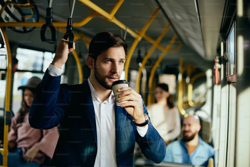 公共交通機関で通勤中に紙コップでコーヒーを飲むビジネスマン。