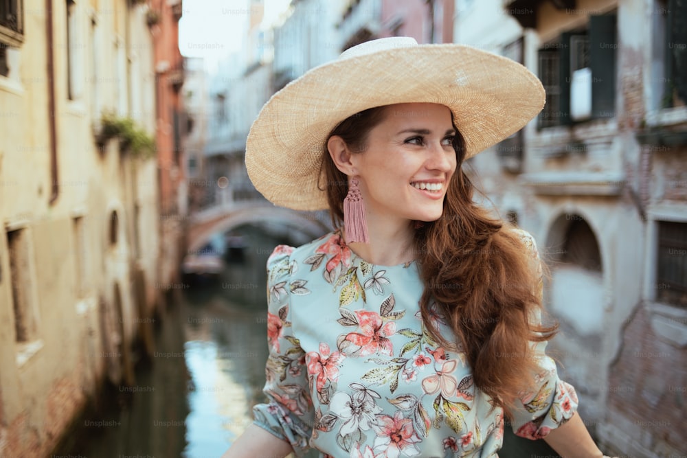 feliz mujer viajera de mediana edad en vestido floral con sombrero explorando atracciones en Venecia, Italia.