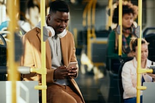 Young black man texting on mobile phone while commuting by bus.