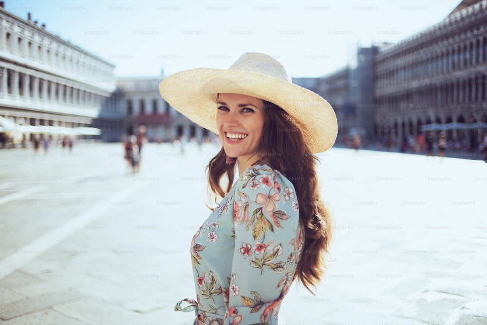 felice donna turista elegante in abito floreale con cappello visita a piazza San Marco a Venezia, Italia.