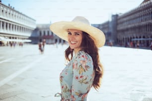 happy stylish tourist woman in floral dress with hat sightseeing at San Marco square in Venice, Italy.