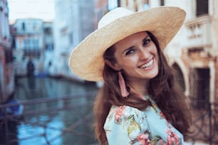 Portrait of happy stylish tourist woman in floral dress with hat sightseeing in Venice, Italy.