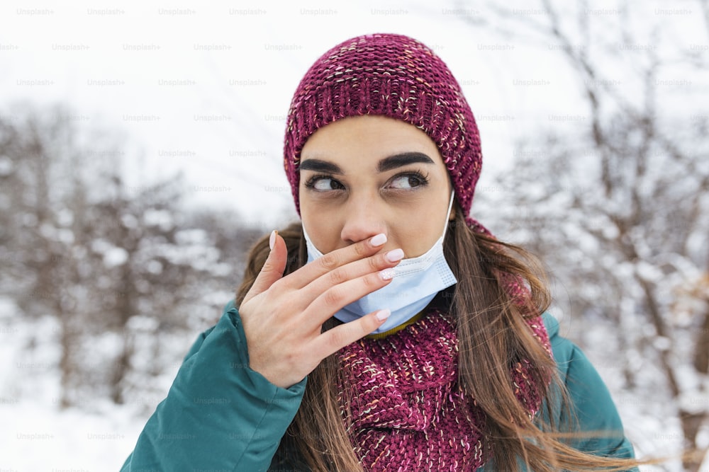 Young woman touching her nose with dirty hand. Avoid touching your nose. Woman wearing face mask rubbing her nose outdoor.Don't touch your face, stop spreading Coronavirus