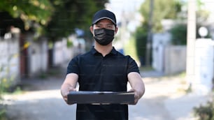 뜨거운 피자가 든 상자를 들고 보호 마스크를 쓴 젊은 아시아 배달원.