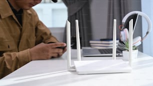 Vista de primer plano de un enrutador inalámbrico con un hombre de negocios que usa una computadora portátil y un teléfono inteligente en el fondo de la oficina en casa.