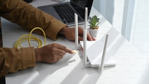 インターネットケーブルをルーターソケットに接続する男のクローズアップビュー。ワイヤレスインターネットのコンセプト。