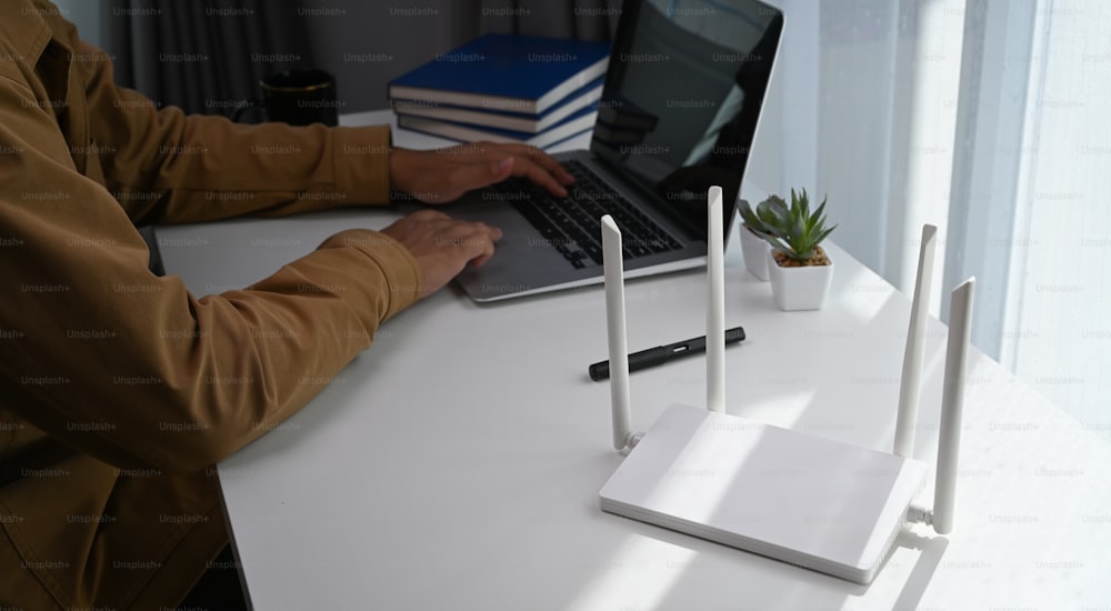 Jeune homme travaillant sur un ordinateur portable et assis devant un routeur Internet sans fil haute vitesse sur son lieu de travail.
