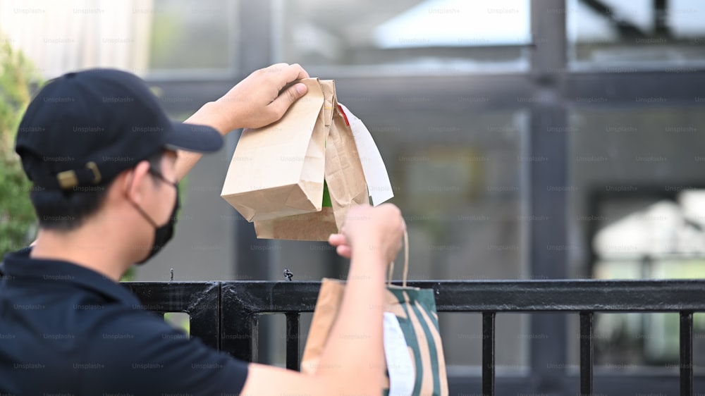 Young Asian delivery man in protective mask delivering food to customer at doorway.