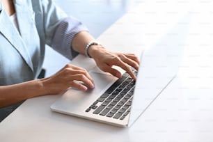 Vista ravvicinata della mano della donna asiatica freelance che lavora o controlla le informazioni dal sito Web sul suo laptop presso la sua postazione di lavoro.