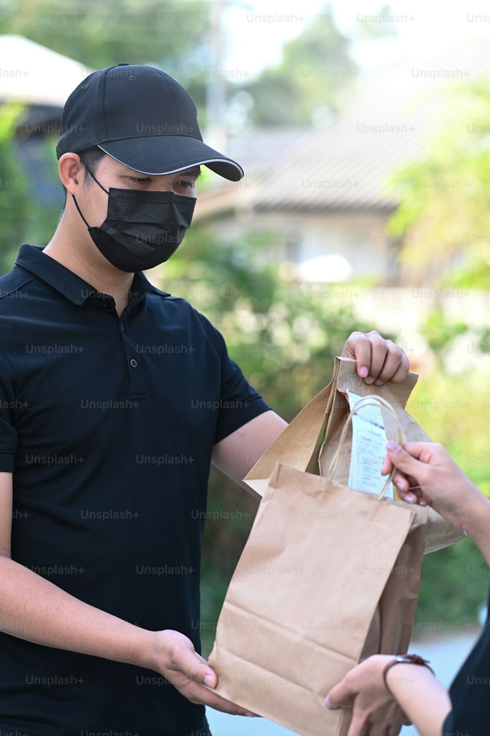 Portrait d’un jeune livreur asiatique portant un masque de protection livrant de la nourriture à un client.
