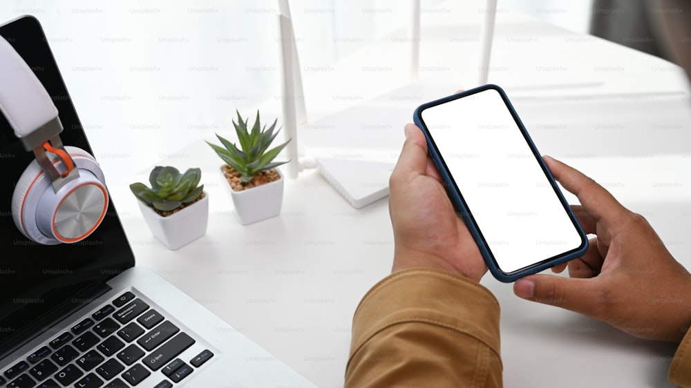 Close up of a man holding smart phone in his hand at workplace with a laptop and wireless router.