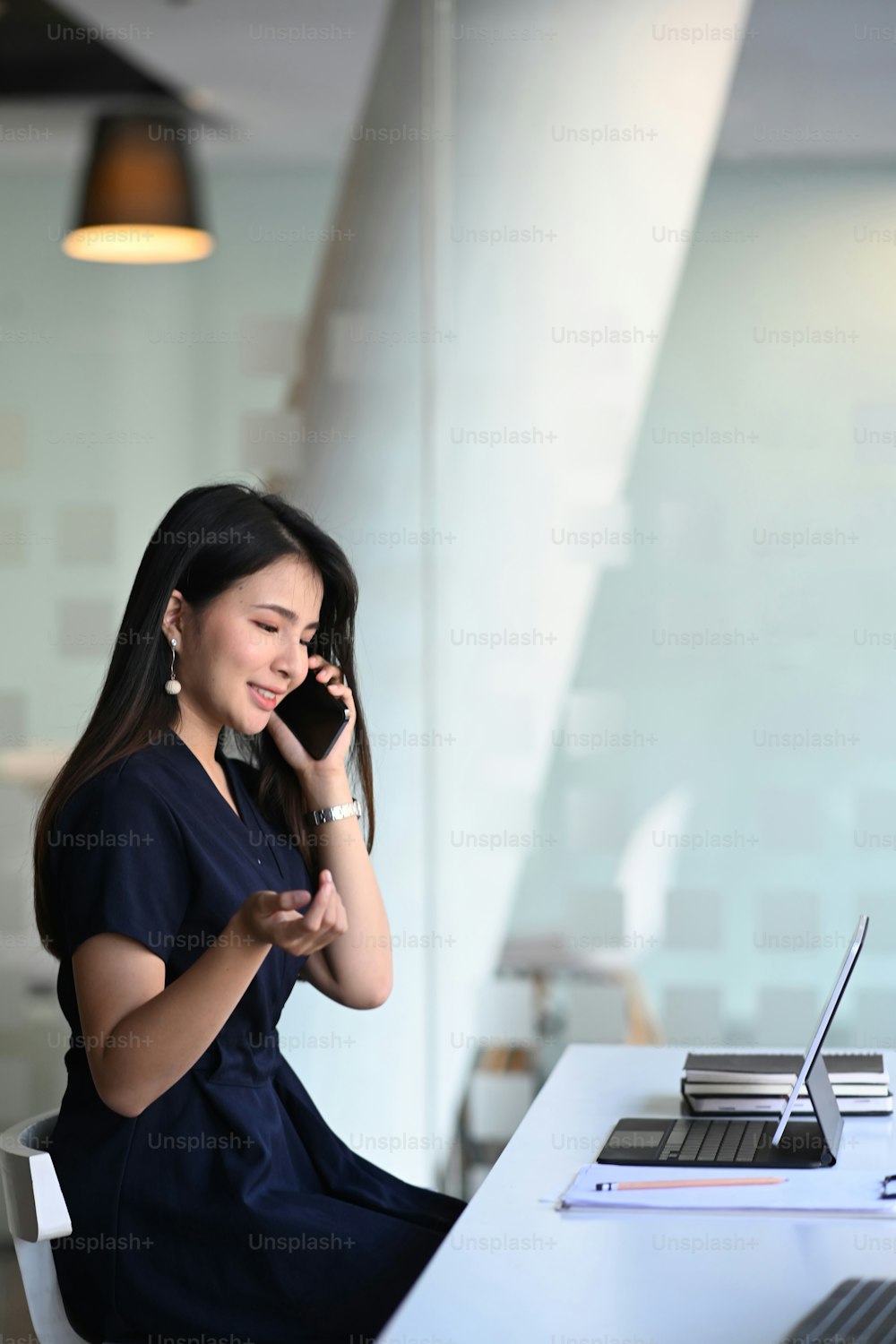 Portrait of young Asian businesswoman sitting at her office desk and talking on mobile phone.