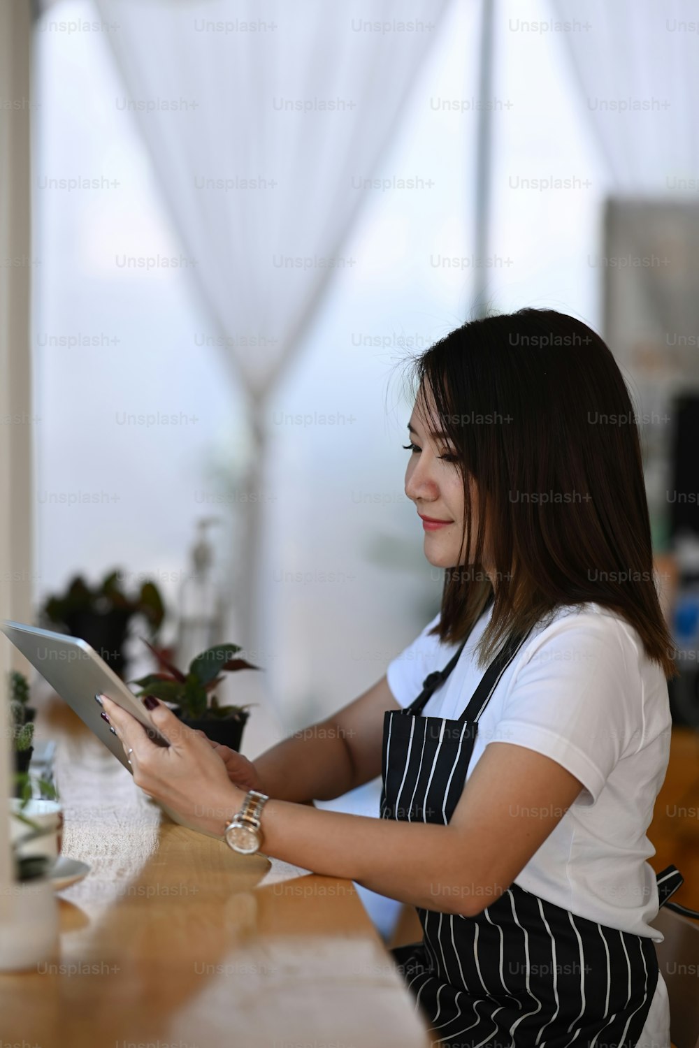 Giovane imprenditrice sorridente che indossa un grembiule seduta in un caffè alla moda e utilizza una tavoletta digitale.