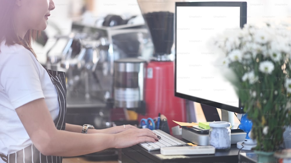 Junge Unternehmerin mit Schürze vor dem Tresen eines angesagten Cafés und am Computer.