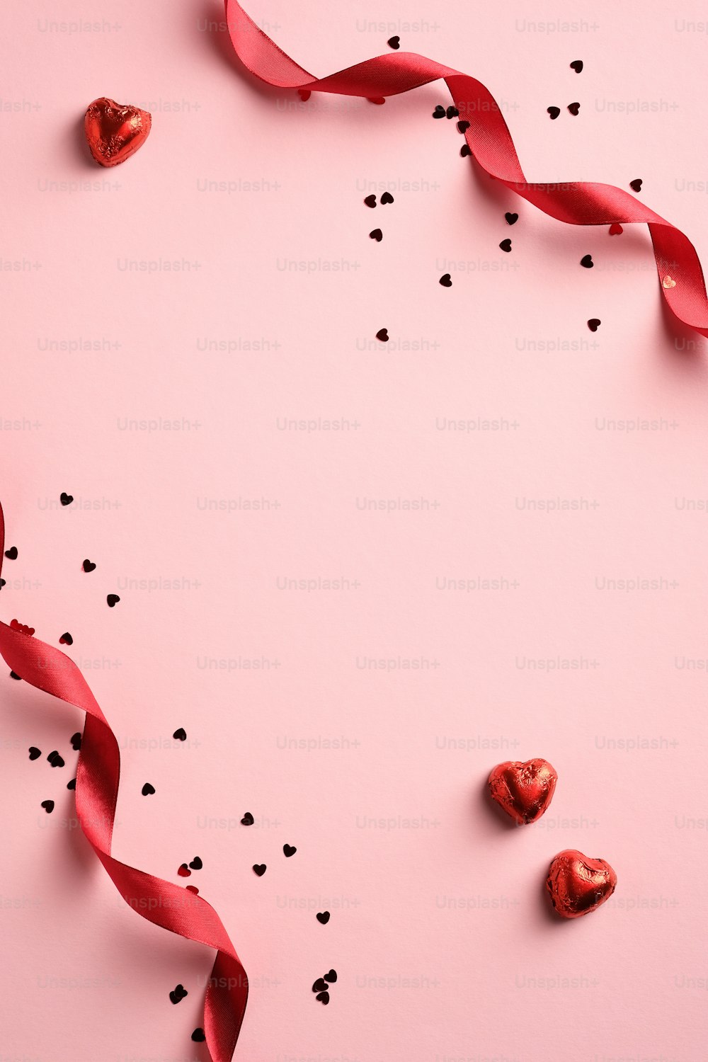 赤いリボン、紙吹雪、ピンクの背景にハート型のお菓子とエレガントなバレンタインデーの背景。ミニマルなスタイル。フラットレイ。