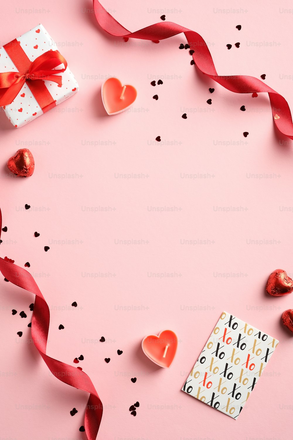 Happy Valentines Day Konzept. Kreatives Layout mit rotem Band, Geschenkbox, Grußkarte, Konfetti auf rosa Hintergrund. Draufsicht, flach gelegt.