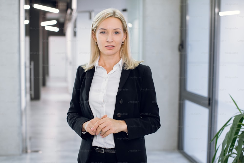 People, business, office concept. Portrait of attractive pleasant confident middle aged businesswoman, financial director, ceo or manager, posing to camera while standing in office hallway interior.