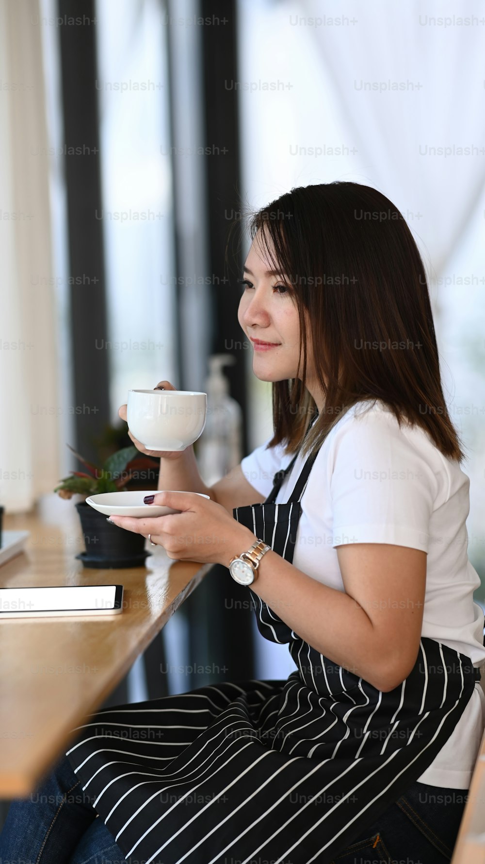 Retrato da dona de uma cafeteria segurando uma xícara de café quente e testando sozinha.