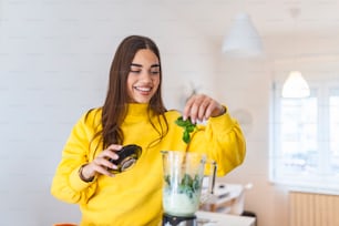 Young woman making detox smoothie at home. Girl making smoothie of fruit and vegetables. Healthy way of life. Happy girl using blender to make smoothie