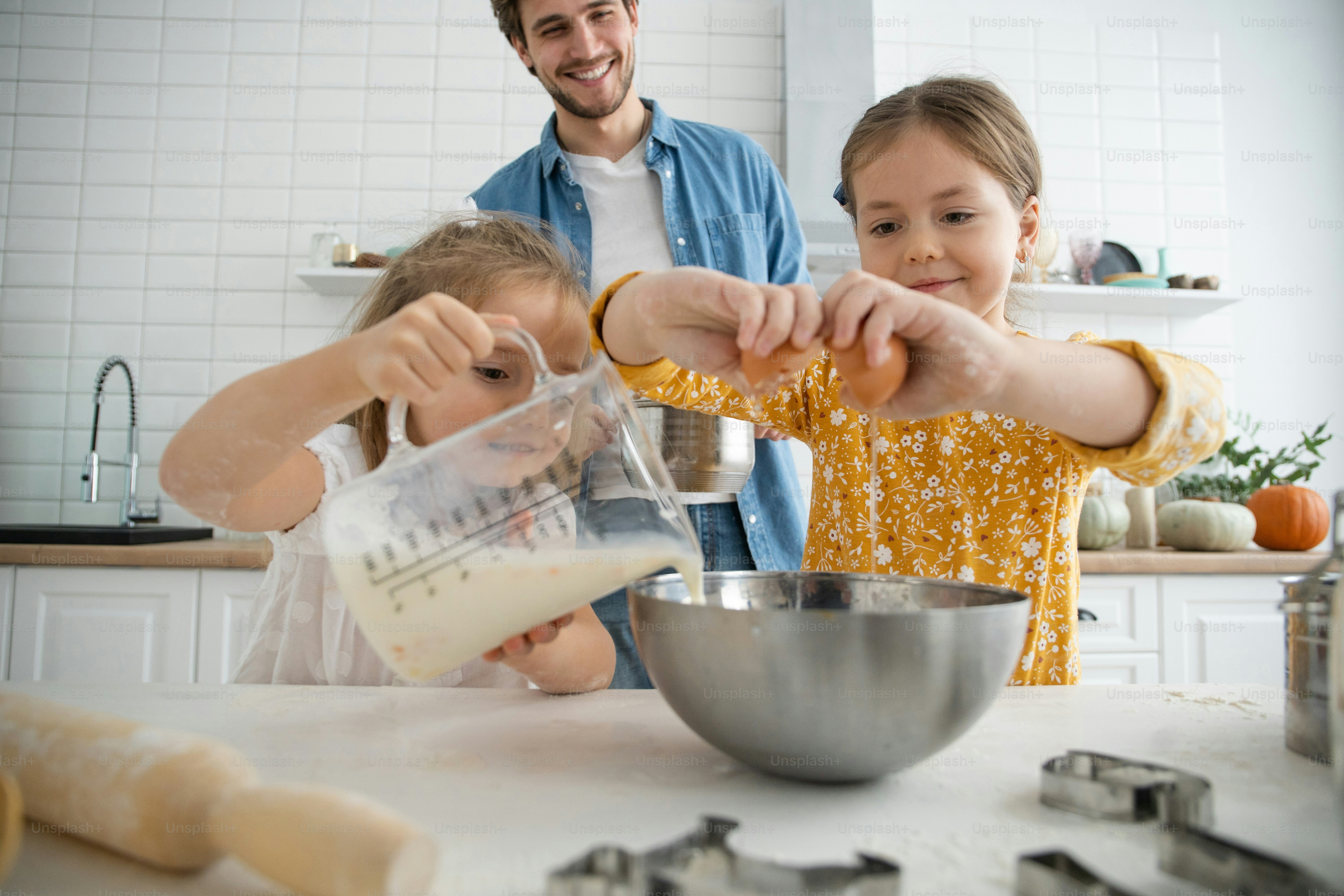 Photo of a smiling father and daughters baking in the kitchen and ...