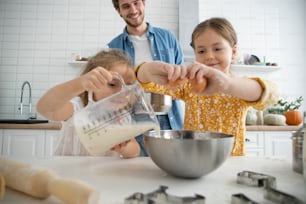 Photo d’un père et de ses filles souriants en train de cuisiner dans la cuisine et de s’amuser.