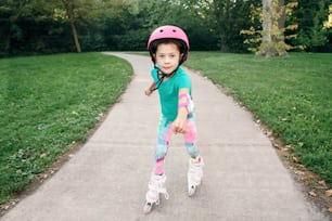Happy Caucasian girl in pink helmet riding in roller skates on road in park on summer day. Seasonal outdoor children activity sport. Healthy childhood lifestyle. Kids individual summer sport.