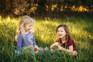 Happy children girls playing dolls in park. Cute adorable kids sitting in grass on meadow playing toys. Happy childhood authentic lifestyle. Outdoor summer backyard activity for kids.