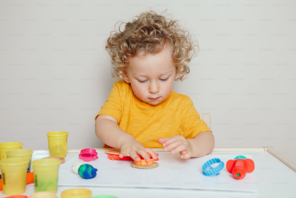 Cute Caucasian blond curly baby boy child playing with sensor kinetic toy playdough. Hand brain development activity for young toddler kids. Early age preschool education.