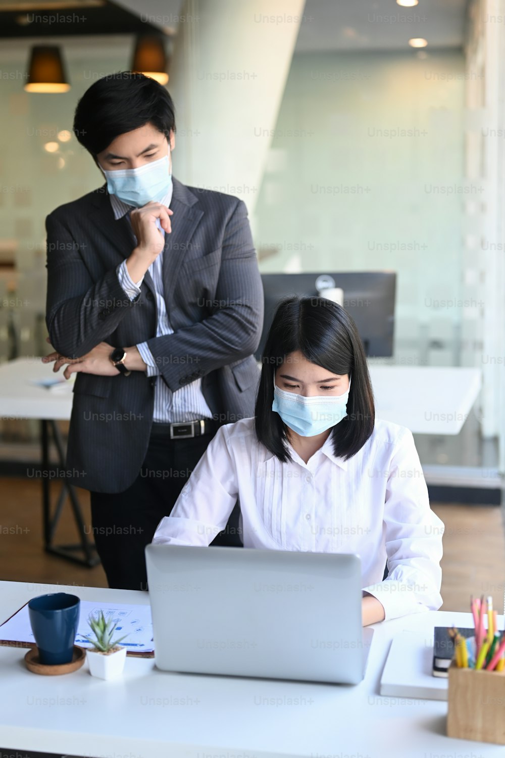 Businesspeople in protective mask analyzing financial figures denoting the progress with laptop at modern office.